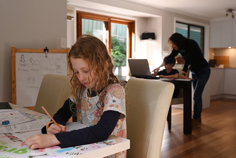 A mother helps her young children learn at home.