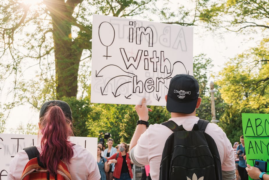Seorang laki-laki memegang poster bertuliskan "Saya bersama (perempuan)" dałam aksi protes terhadap putusan Mahkamah Agung Amerika Serikat untuk mencabut hak aborsi.