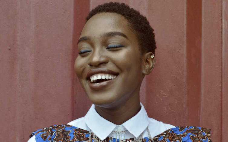 Woman against a wall closing her eyes and smiling