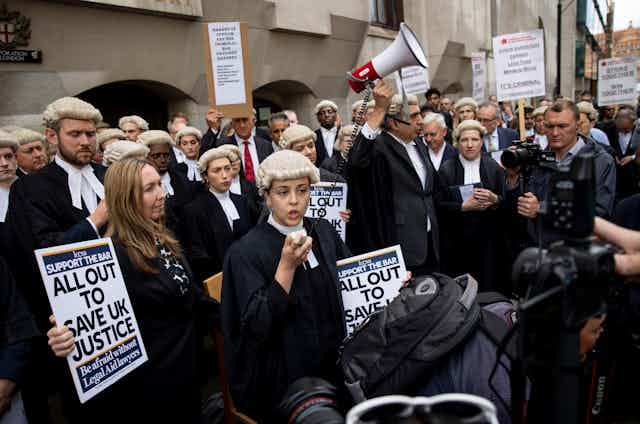 A group of young barristers in their wigs and gowns, many holding protest signs, one holding up a megaphone
