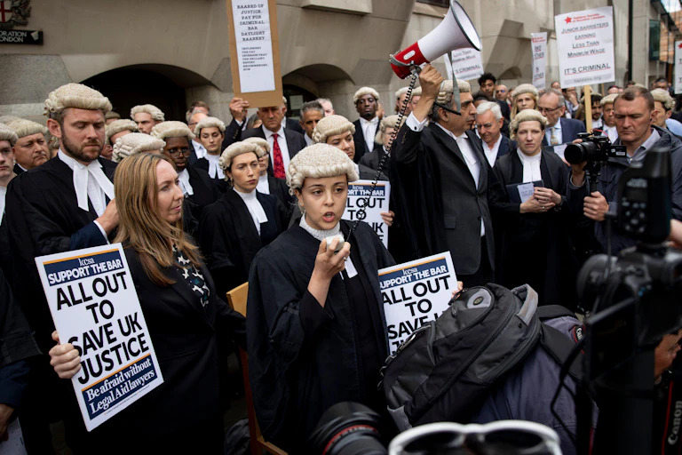 A group of young barristers in their wigs and gowns, many holding protest signs, one holding up a megaphone