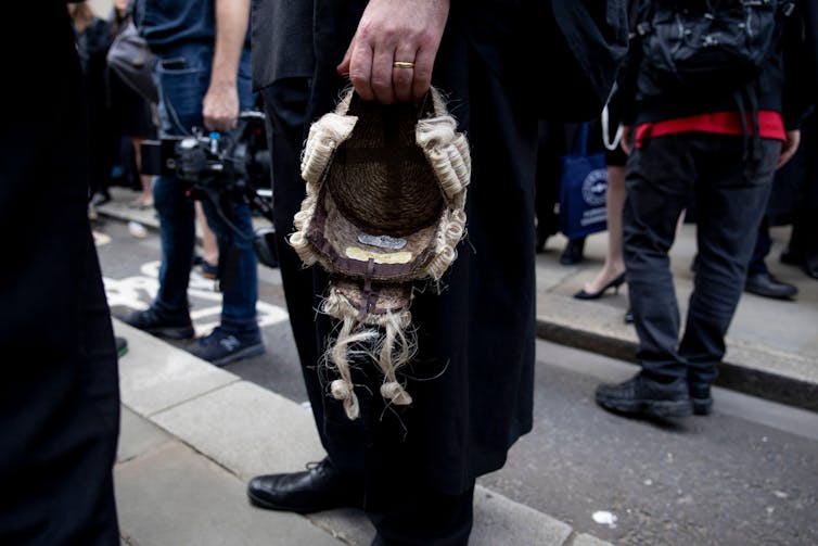 A close up of a barrister's hand holding his wig down by his side