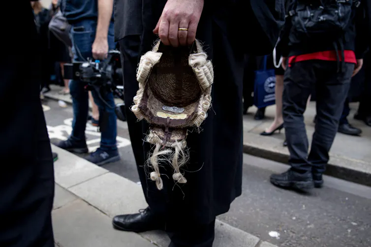 A close up of a barrister's hand holding his wig down by his side
