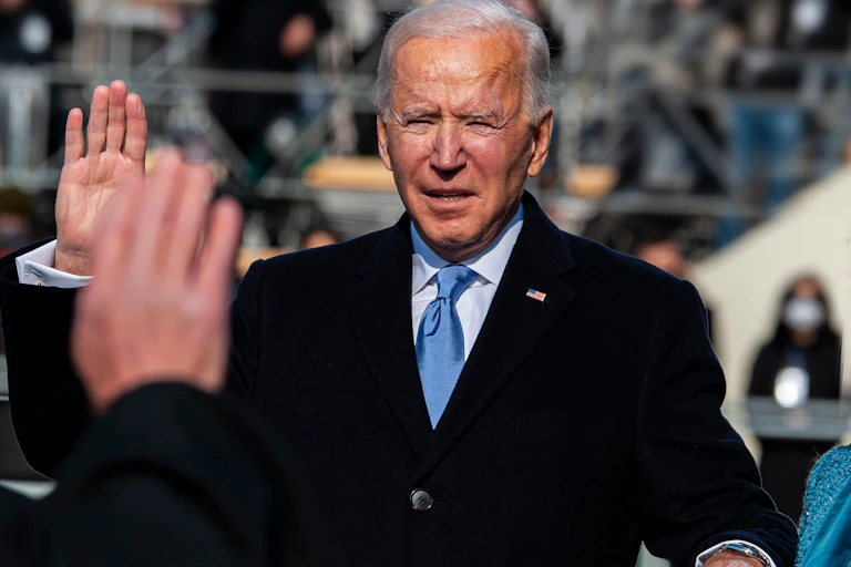 Joe Biden with his right hand raised, squinting into the sunlight as he is sworn in.