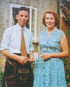 A young man in a kilt and a young woman in a summer dress standing in a garden in the 1950s.