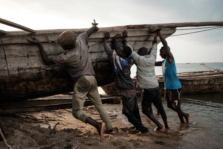 Quatre hommes poussent une barque sur une plage