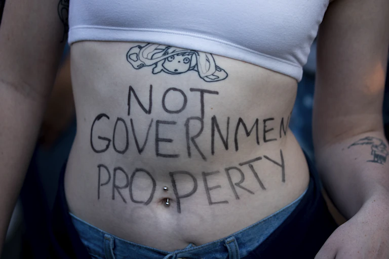 A woman with writing on her abdomen reading 'not government property'.