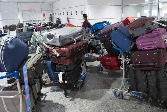 Hundreds of bags of luggage are stacked on carts as a man in the background searches for his bags.