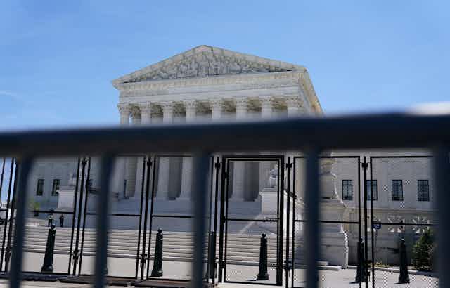 An ornate court building is seen behind black security fencing.