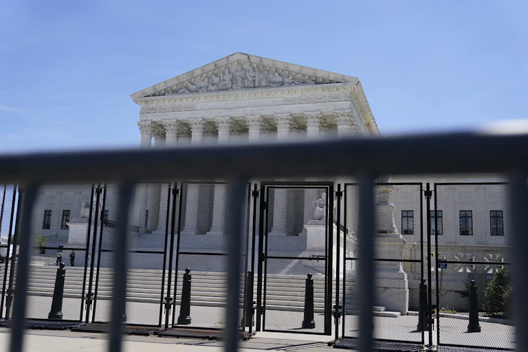 An ornate court building is seen behind black security fencing.