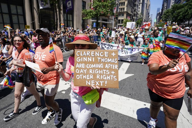 A woman in a parade holds a sign that reads Clarence Thomas and Ginni Thomas are coming after gay rights next