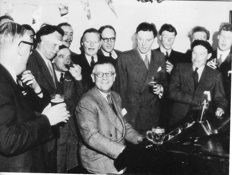 A man at a piano surrounded by second world war RAF servicemen recovering from burns injuries suffered in action.