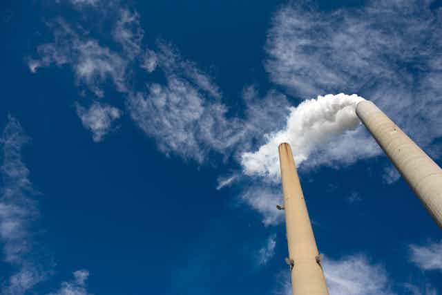 Two smokestacks vent white clouds into a blue sky