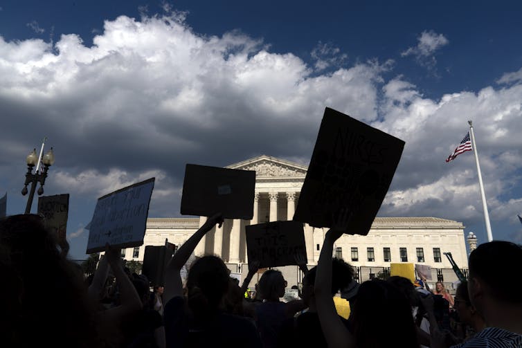 silhouettes of protesters with signs in front of supreme court building