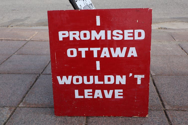 a sign with white letters on a red background reading I PROMISED OTTAWA I WOULDN'T LEAVE