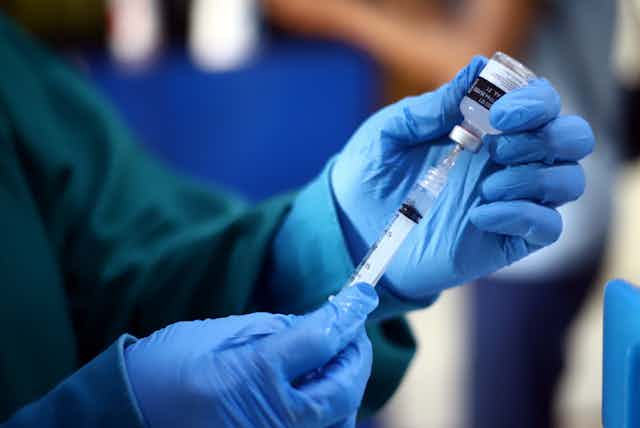 A healthcare worker wearing gloves draws up a vaccine.