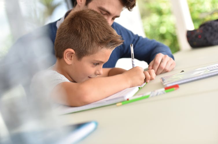 Un hombre ayudando a un niño a hacer deberes escolares.
