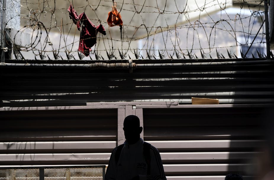 The silhouette of a man in shadow in seen in front of a barrier with barbed wire  and spikes.