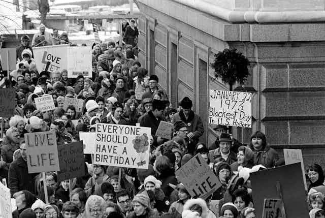 Protesters from a 1973 photo hold up placard saying, 'Everybody should have a birthday,' January 22, 1973, blackest day in US history,' 'Love Life,' among others.