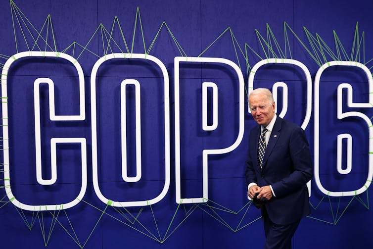 Biden walks in front of a large screen reading 'COP 26'