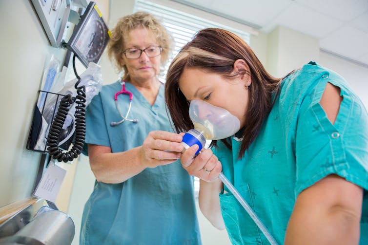 Woman with a gas mask inhaling with assistance from nurse