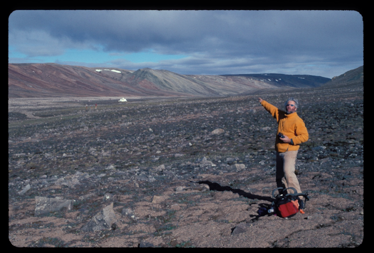 Un hombre de pie sobre un suelo rocoso plano con montañas en la distancia