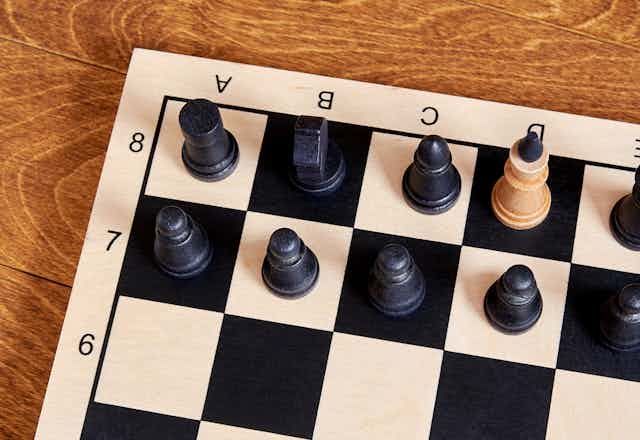 Chessboard with one white piece among black pieces. 