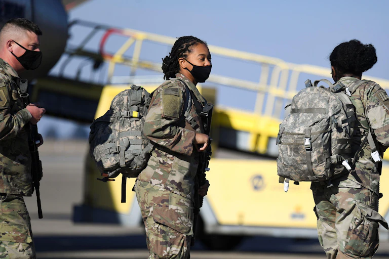 Four soldiers in khaki exiting a plane.