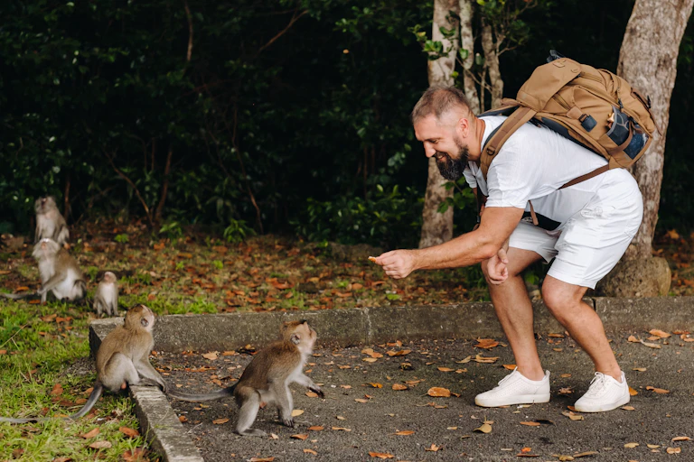 Un homme avec un sac à dos qui tend à manger à un petit singe.