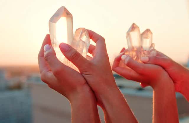 Two sets of hands hold crystals over a balcony at sunset.