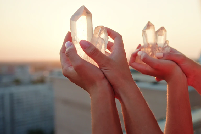 Two sets of hands hold crystals over a balcony at sunset.