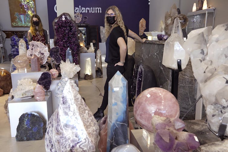 Two masked women walk through a store filled with colorful crystals.