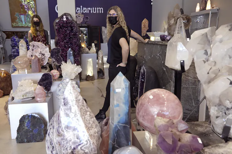 Two masked women walk through a store filled with colorful crystals.
