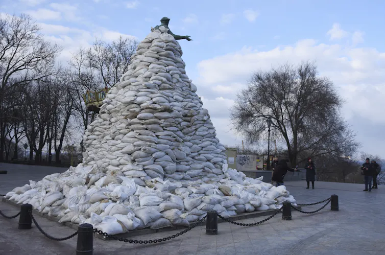 a tall statue of a man with his arms outstretched is covered in sandbags