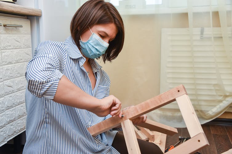 a woman in a mask wearing a blue shirt puts together furniture