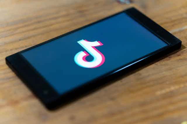 TikTok logo is shown on a mobile on a wooden table 