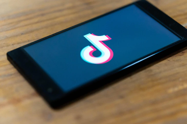 TikTok logo is shown on a mobile on a wooden table