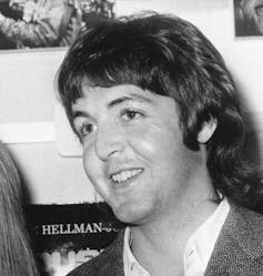 A man in a white shirt unbuttoned at the top collar smiling.