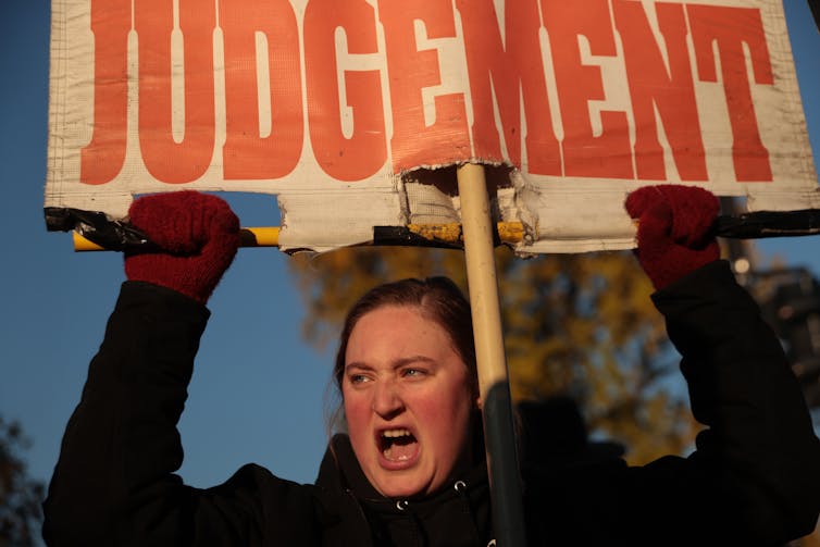 A white woman shouts as she holds up a sign that reads 'Judgment'.