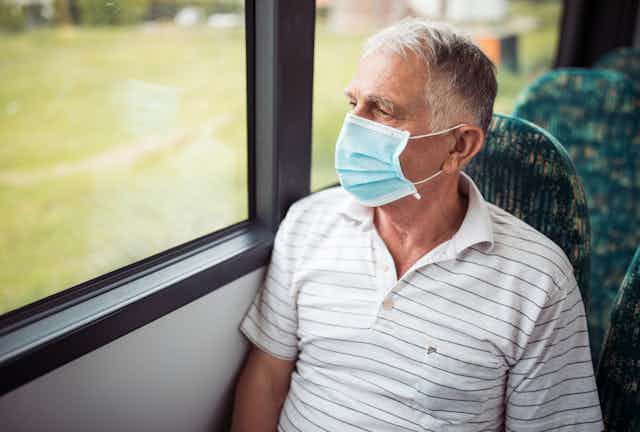 Older man in a mask riding a bus looks out the window