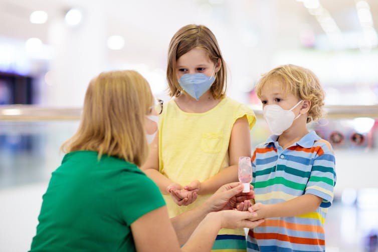 Mother puts sanitiser on her masked kids' hands