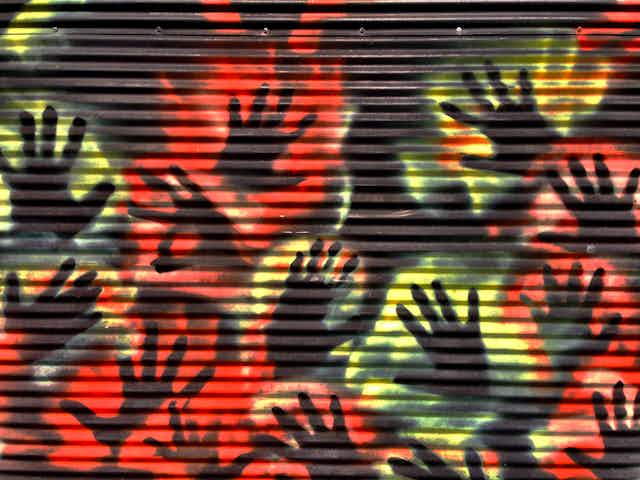 A corregated iron wall with stencilled hands in red and yellow.