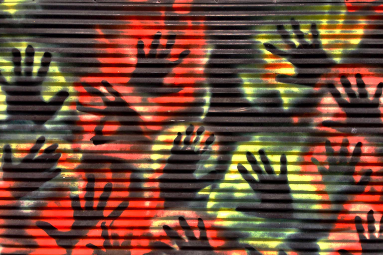A corregated iron wall with stencilled hands in red and yellow.