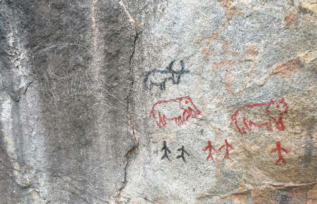 Red and black drawings of animals and people on a rock surface