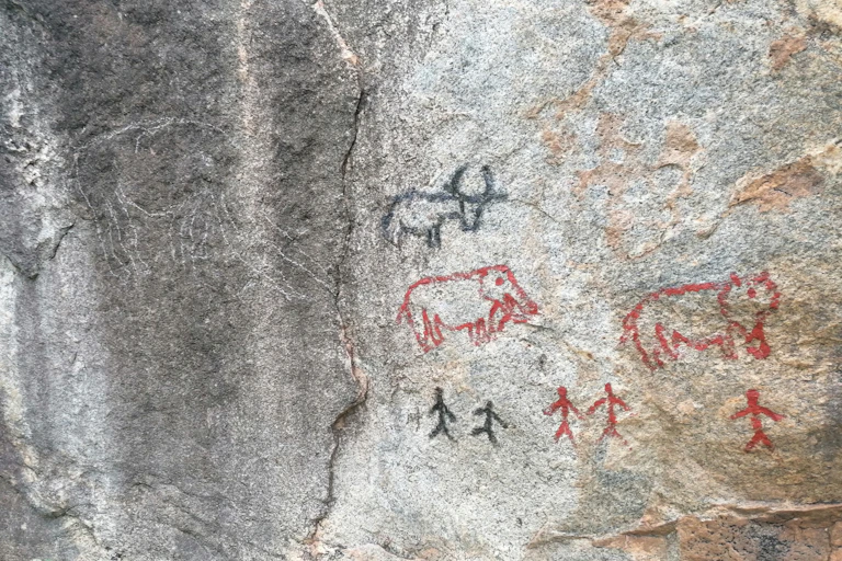Red and black drawings of animals and people on a rock surface