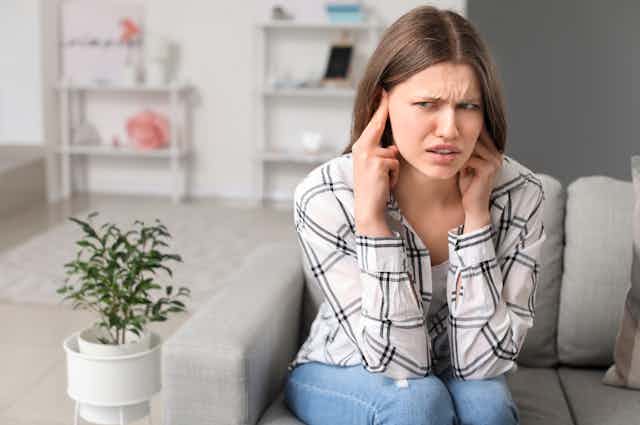 Una mujer con gesto contrariado, de molestia, se toca los oídos con las manos