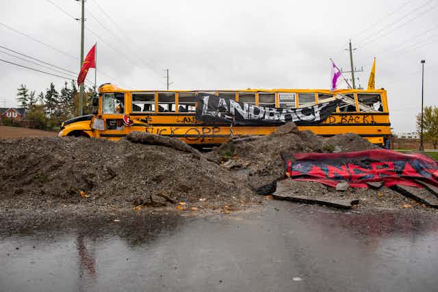 A bus is blocking a road and reads 'land back'