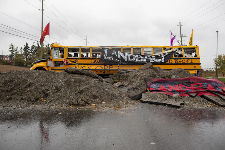 A bus is blocking a road and reads 'land back'