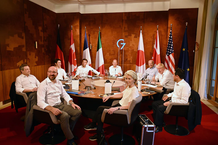 A group of formally dressed people seated around a table with microphones in front of each of them.