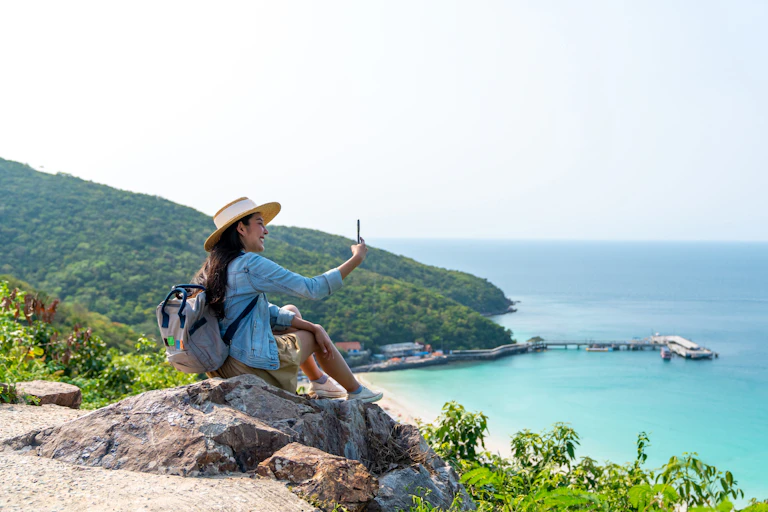 A woman takes a selfie overlooking a beach.